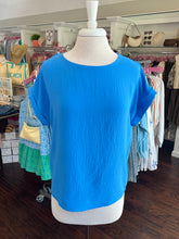 Bright colbalt blue top on a mannequin in a store setting with various items in the background