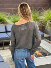 Person wearing a gray patterned sweater and blue jeans standing outdoors near a fire pit.