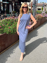 Woman in a sleeveless blue dress standing outdoors with flowers and tables in the background