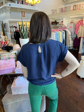 Woman wearing a short sleeve navy blouse showing the back view  standing in a store.