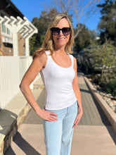 Woman wearing a white sleeveless top and light blue jeans standing outdoors.