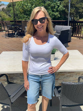 Woman wearing sunglasses and a white shirt standing outdoors on a patio.