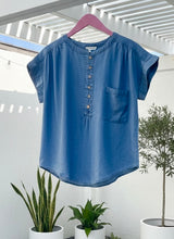 Chambray Henley SS Top on a hanger with plants in the background
