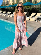 Woman in a pink dress standing by a poolside with lounge chairs and umbrellas in the background.