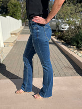 Person wearing blue slim bootcut jeans standing on a sidewalk.