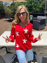 Woman wearing a red sweater with white stars, standing outdoors on a patio.