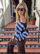 A woman wearing a brown and light blue striped knit sweater and brown pants, sitting on outdoor tiled steps.