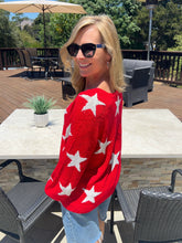 Woman wearing a red sweater with white stars outdoors on a wooden deck.
