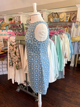 Mannequin wearing a blue patterned dress with a rack of hanging clothes in the background.