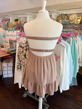 Mannequin wearing a beige dress with a rack of clothes in the background