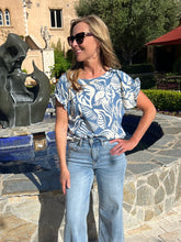 Woman in a blue and white patterned top and jeans standing outdoors near a sculpture.