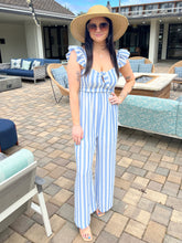 Woman in a blue and white striped jumpsuit standing in an outdoor patio area.
