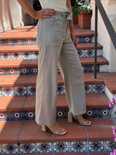 A person wearing light beige wide-leg cropped pants with a matching tie belt, styled with beige block-heel sandals, standing on terracotta tiled stairs with blue patterned tile accents.