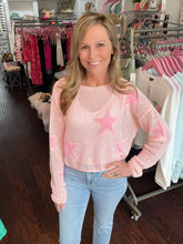 Woman wearing a pink sweater with star patterns in a clothing store.