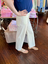 Person wearing a blue shirt and white pants in a store setting with clothing racks in the background.
