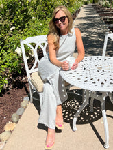Woman sitting at a white outdoor table and chair set, holding a cup.