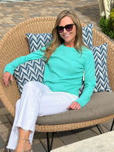 Woman sitting on a wicker chair with chevron patterned cushions, wearing sunglasses and a teal top.