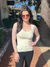 Woman wearing a white tank top and sunglasses outdoors on a sunny day.