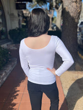Person wearing a white long-sleeve top and black pants outdoors.