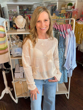 Woman wearing a beige sweater and blue jeans standing in a clothing store.