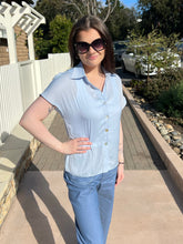 Woman wearing a halogen blue top and pants standing outdoors on a sidewalk.