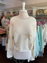 White sweater with star patterns on a mannequin in a store setting.