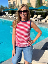 Woman in a red and white striped shirt and blue shorts standing by a pool.