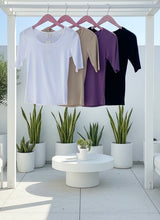Four ribbed tees on hangers with plants and a white table in the background