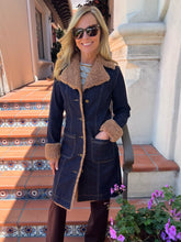 A woman wearing a dark navy blue denim-style coat with a tan shearling-style collar, cuffs, and hem, standing on tiled outdoor steps.