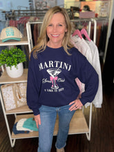 Woman wearing a navy sweatshirt with 'Martini Social Club' text in a store setting