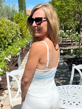Woman in a white dress with thin straps standing in a garden setting.