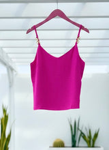 Fuchsia tank top on a hanger against a white wall with plants in the background