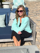 Woman sitting on a blue outdoor sofa wearing sunglasses and a light mint cardigan.