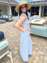 Woman in a blue and white striped jumpsuit and sun hat standing on a patio.