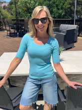 Woman in a blue shirt and denim shorts standing outdoors on a patio.