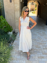Woman in a white dress standing on a stone path with plants and a building in the background