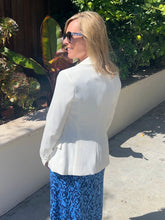 Woman wearing a white blazer and blue patterned dress outdoors.