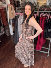 A woman modeling a strapless snake-print midi dress in a clothing boutique, standing in front of racks of other garments.