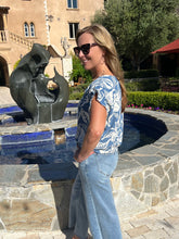 Woman standing by a sculpture in an outdoor setting with a building and trees in the background