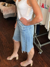 Person wearing a white tank top and light blue denim shorts in a store setting.