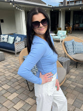 Woman in a blue top and white pants standing outdoors on a patio.