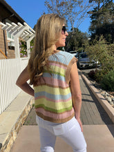 Woman wearing a colorful striped sweater vest standing on a sidewalk.