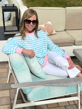 Woman sitting on a chair with a pillow, wearing a striped shirt and sunglasses, outdoors.