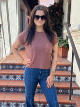A woman wearing a short-sleeve ribbed knit top in dusty rose pink and blue jeans, standing on tiled outdoor stairs.