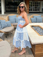 Woman in a blue floral dress standing outdoors near patio furniture.
