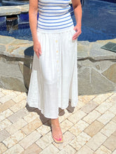 Person wearing a striped top and white skirt standing by a pool.