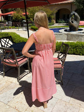 Woman in a pink and white striped dress standing in an outdoor setting with chairs and a fountain.