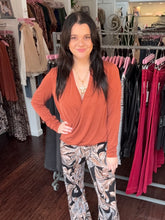 A woman modeling a rust-orange long-sleeve wrap top and black-and-white patterned pants inside a clothing boutique.