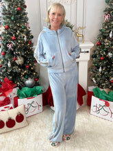 Woman in a blue sporty velour tracksuit set standing in a festive room with Christmas trees and presents.