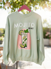Light green sweatshirt with 'MOJITO MINT' design on a hanger outdoors.